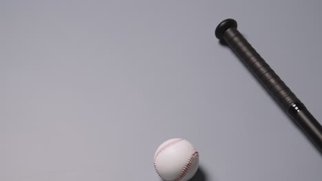 overhead baseball still life with bat and ball rolling into frame against grey background