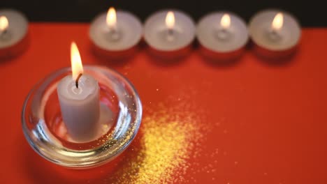 Burning-white-candles-on-a-red-background,-falling-gold-dust