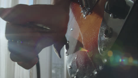beautiful slow motion shot connecting a plus cable to a fender jaguar electric guitar inside a room as sunlight streams in through the balcony.