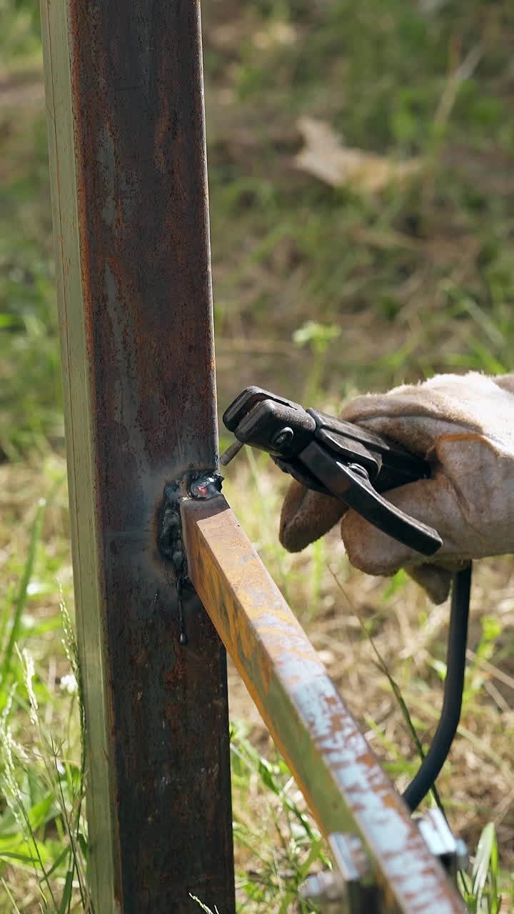 closeup repairman fixes neatly part of future metal fence using welding machine in summer garden