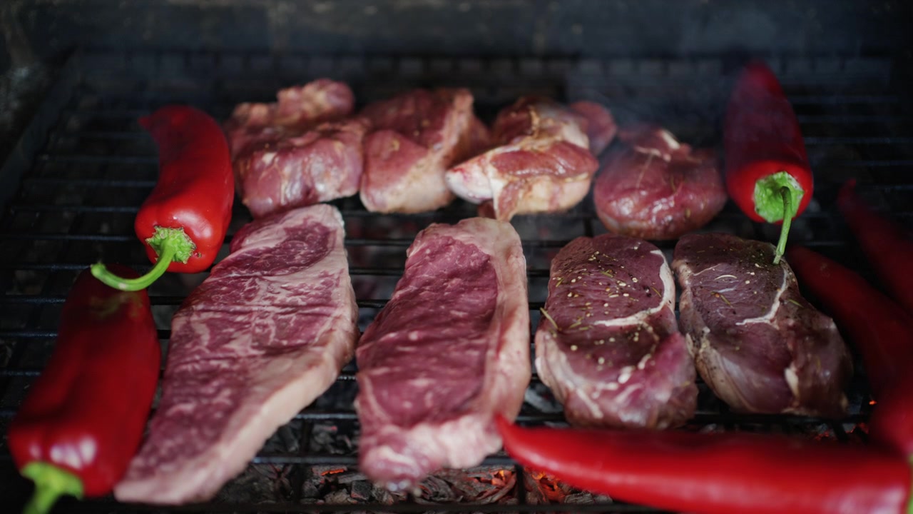 Carne che cuoce su una griglia con melanzane e peperoni rossi, con del fumo che sale