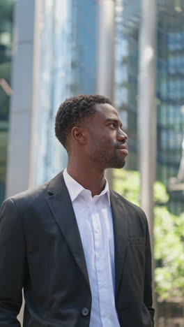 Vertical-Video-Of-Young-Businessman-Wearing-Suit-Standing-Outside-Looking-Up-At-Offices-In-The-Financial-District-Of-The-City-Of-London-UK-Shot-In-Real-Time