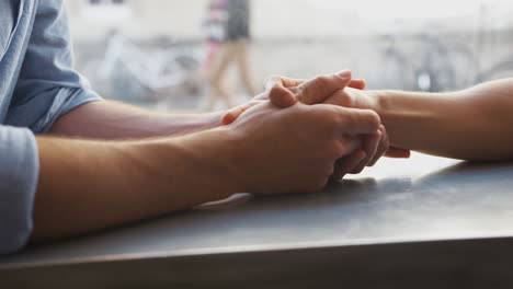 un primer plano de una pareja de hombres homosexuales que se toman de la mano en una cafetería.