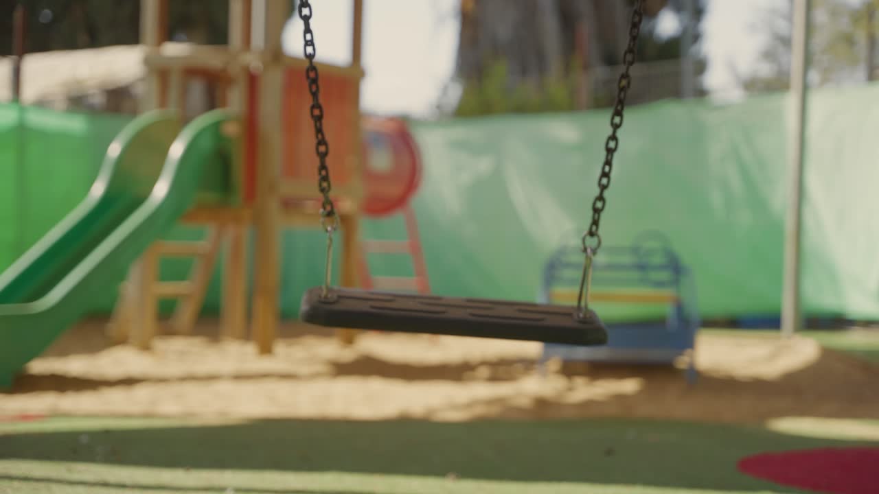 Empty swing moves gently in sunny playground with no children around. School or Kindergarten closure, neglect, missing child, bullying aftermath, or about safety concerns , supervision, child welfare