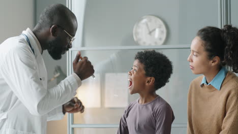 Black-Pediatrician-Examining-Throat-of-Boy-with-Flashlight