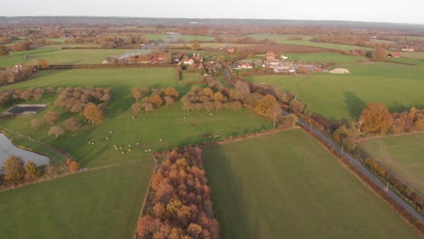 Eine-Herbstluftaufnahme-Von-Südengland-Mit-Einem-Dorf,-Ackerland,-Einem-Wald,-Einem-See-Und-Feuerrauch-Aus-Einem-Schornstein