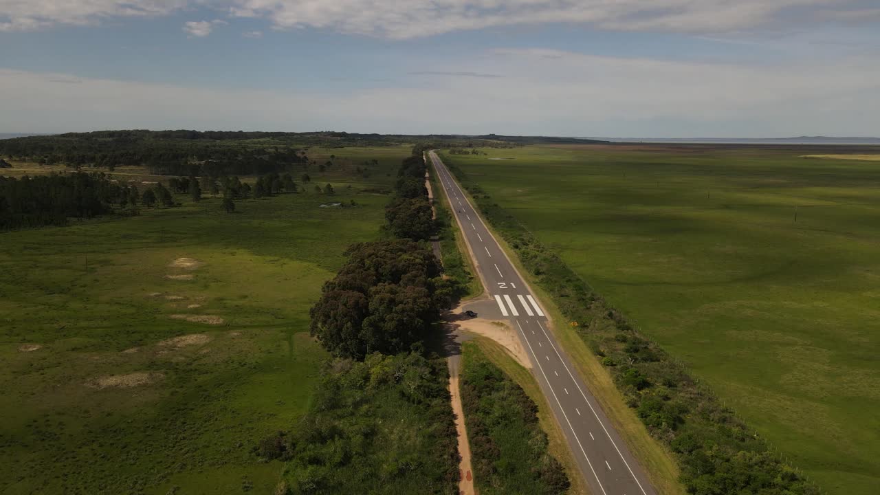 toma aérea hacia atrás de una pista de aterrizaje de emergencia en un camino rural en uruguay durante el día soleado