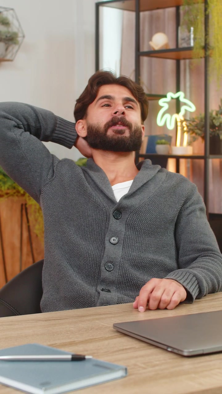 Un uomo indiano finalizza una relazione sul laptop, preme invio, chiude lo schermo, sorride, sollievo, lavoro terminato, è ora di riposare