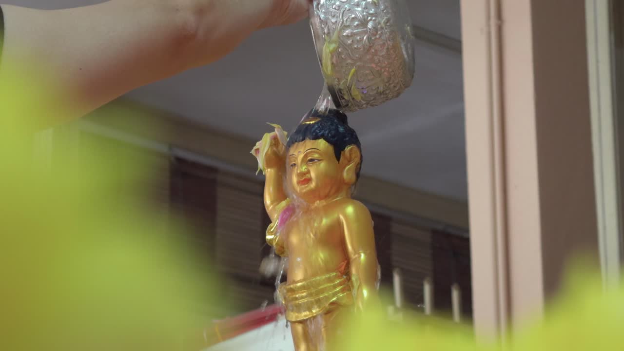 A devotee pours water over a golden baby Buddha statue during the Vesak Day ritual, symbolizing purification and reverence in a traditional Buddhist ceremony.