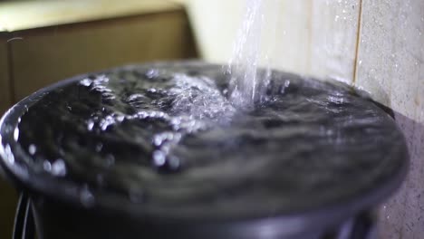 old faucet filling the bucket with a jet of water overflowing