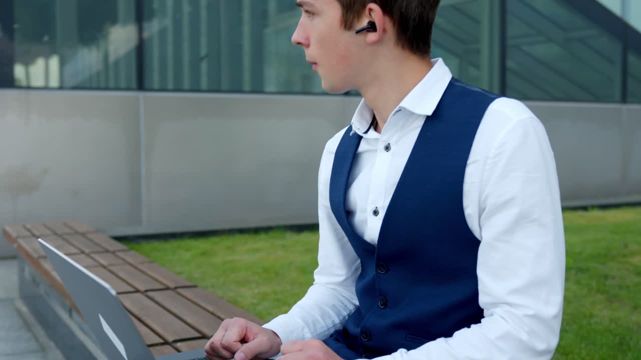 A Young Finance Analyst Works on His Laptop While Listening to Music Outdoors - Orbit Shot