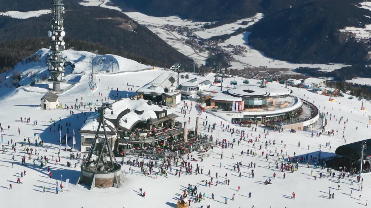 Aerial view of the Kronplatz mountain, the Dolomites, Italy. Concordia bell is ringing, hundreds of skiers move on the plateau. It is sunny, the sky is clear, the valley below is covered with snow.