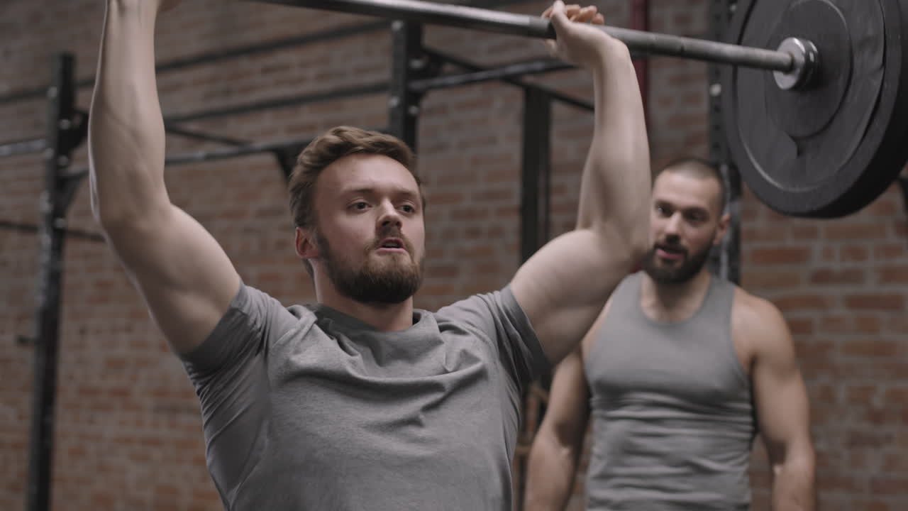 Coach Watching Sportsman Lifting Barbell in Gym