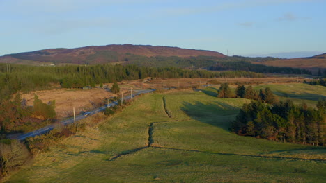 A wide establishing of rolling hills and open fields stretches under a cloudy sky, with a distant river, Irish countryside