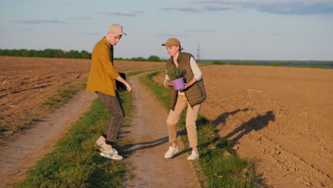 two people on a country road in a field, with a plant