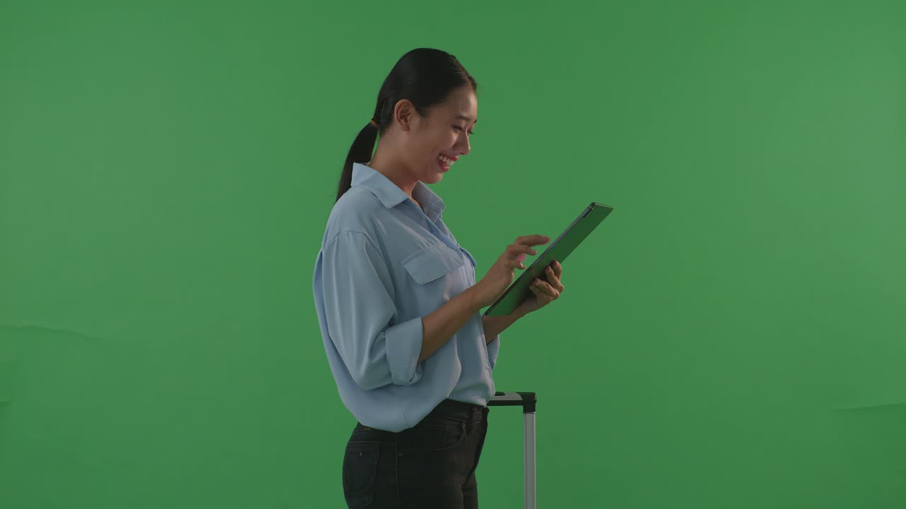 측면 뷰 아시아 여성 여행자가 짐을 들고 태블릿을 사용하는 동안 축하하고 녹색 화면 배경 스튜디오에서 해가 지는 시간