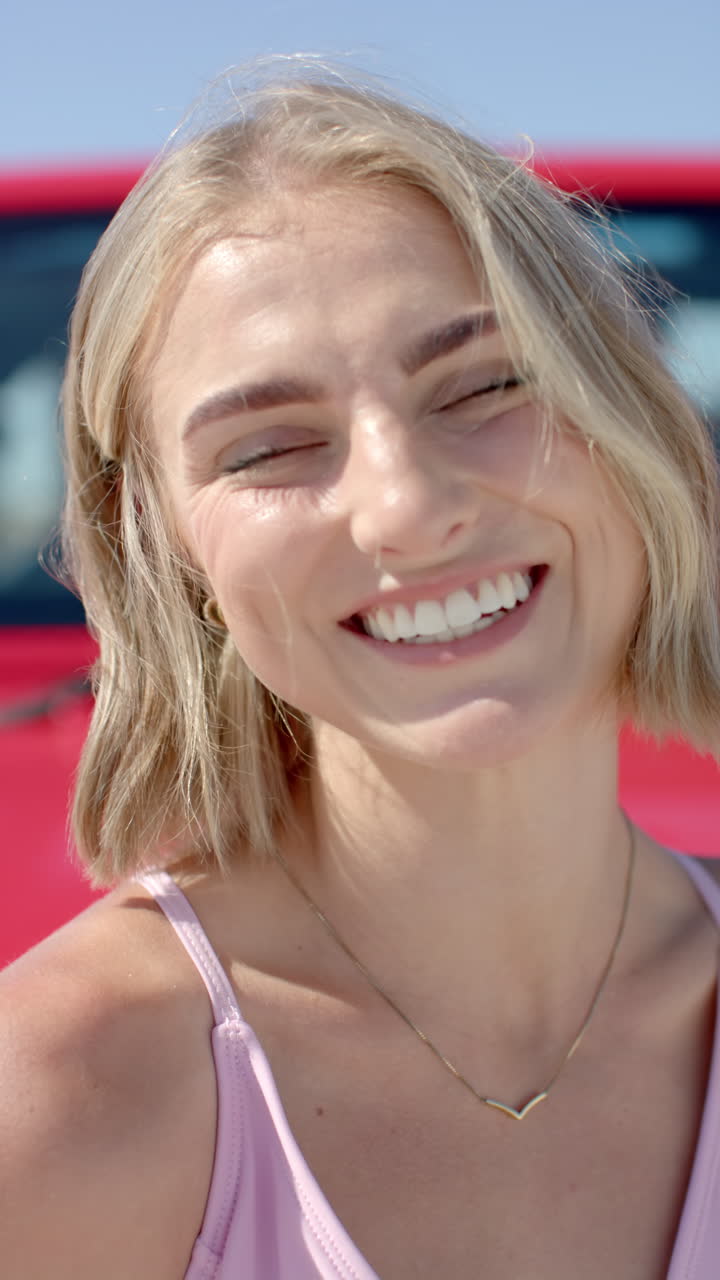 Vertical video: Smiling woman enjoying road trip with red car in background
