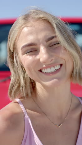 vertical video: smiling woman enjoying road trip with red car in background