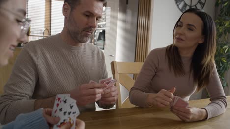 Mid-shot-of-caucasian-family-of-parents-and-teenage-girl-playing-cards-by-the-table