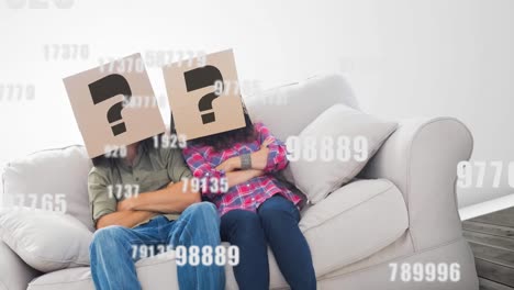 Animation-of-growing-numbers-and-question-marks-over-caucasian-couple-sitting-on-sofa