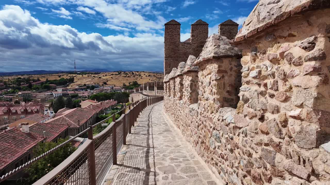 Vista a lo largo de las famosas murallas medievales de Ávila, España. Un camino de piedra recorre junto a históricas almenas con vistas al casco antiguo, mostrando una de las fortificaciones mejor conservadas de Europa