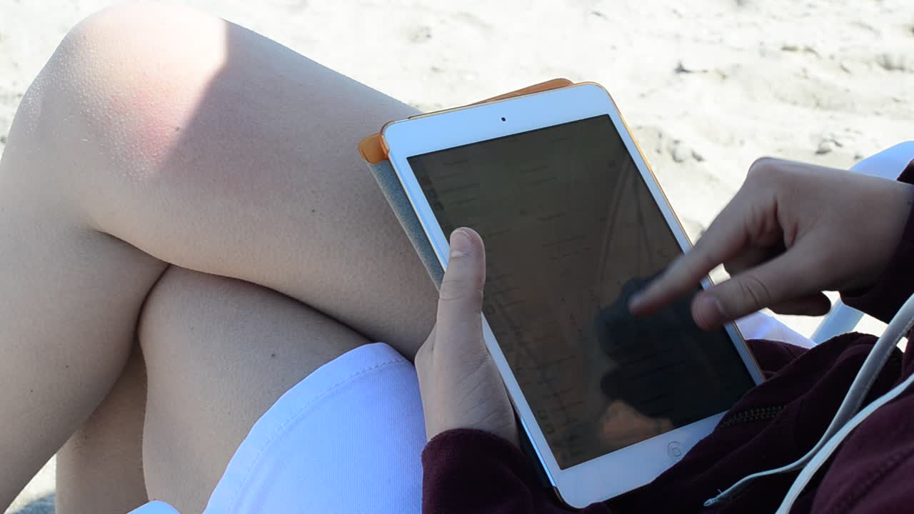 Tabletten i pigens hænder på stranden. Arbejde på tabletten. Optagelse på stranden