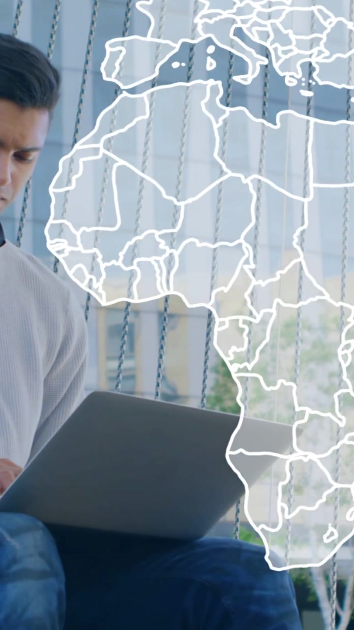 Vertical video: Man raising phone while map overlay appearing over blinds showing laptop for tech