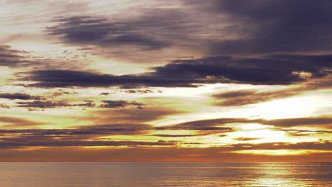 golden sunrise timelapse, sun rising over calm sea through clouds, wide shot