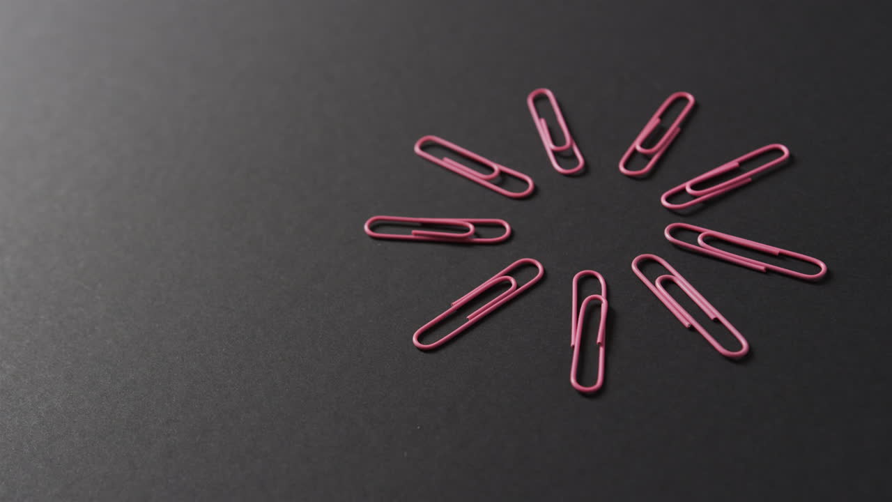 Pink paper clips are arranged in a circular pattern on a black background, with copy space