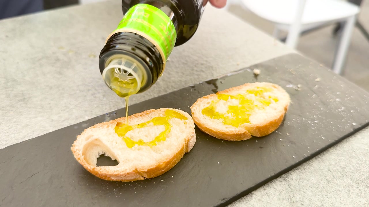 レストランで、手がボトルから黄金色のオリーブオイルを焼きたてのパンに注いでいる。