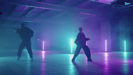 two hip-hop dancers in neon light dance together in blue and purple colors.