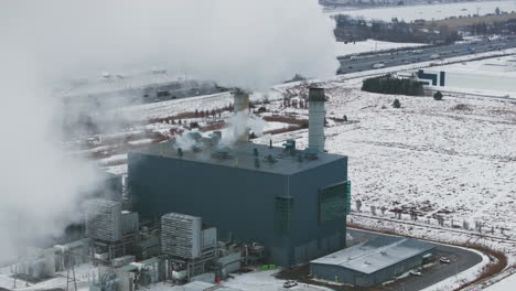 industrial plant with smokestacks in winter, smoke billowing into sky, snow-covered ground, aerial view