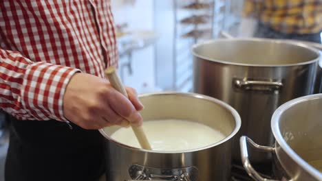 close up of hand of chef stirring the pot of delicious soup on the stove while wearing traditional south german outfit for oktoberfest