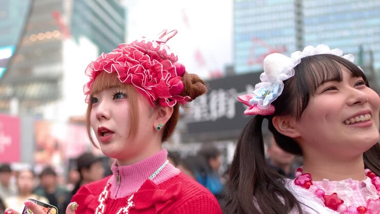 Due donne vestite alla moda decora con colori rosa e rosso vivaci ridono insieme in una città affollata.