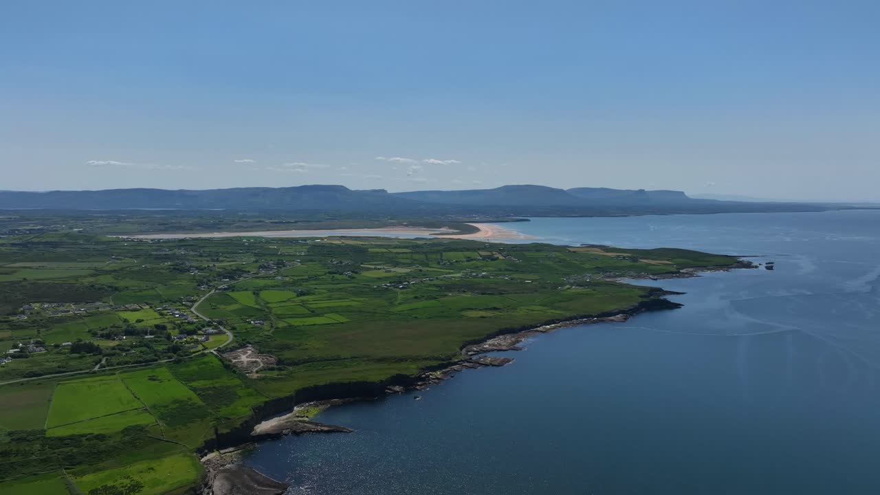 Tullan Strand,, County Donegal, Ireland, June 2023. Drone pulls backward and descends above the blue water at Rossnowlagh while facing south with the Sligo Mountains in the distance.