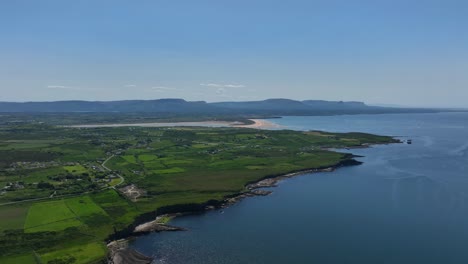 Tullan Strand,, County Donegal, Ireland, June 2023. Drone pulls backward and descends above the blue water at Rossnowlagh while facing south with the Sligo Mountains in the distance.