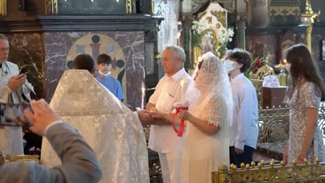 Ukraine,Kyiv,St Volodymyr Cathedral's interior during a wedding ceremony,Priest holding hands of the bride and groom, holding candles, he walks them towards to him and turns around,starts the ceremony