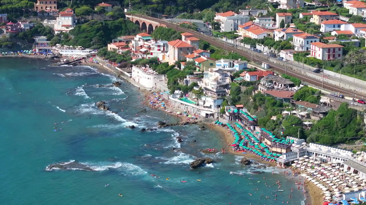 Onde mediterranee lambiscono le spiagge di Castiglioncello, Italia; stabilimenti balneari e caratteristici hotel boutique punteggiano la costa dell'Europa ad alto reddito.