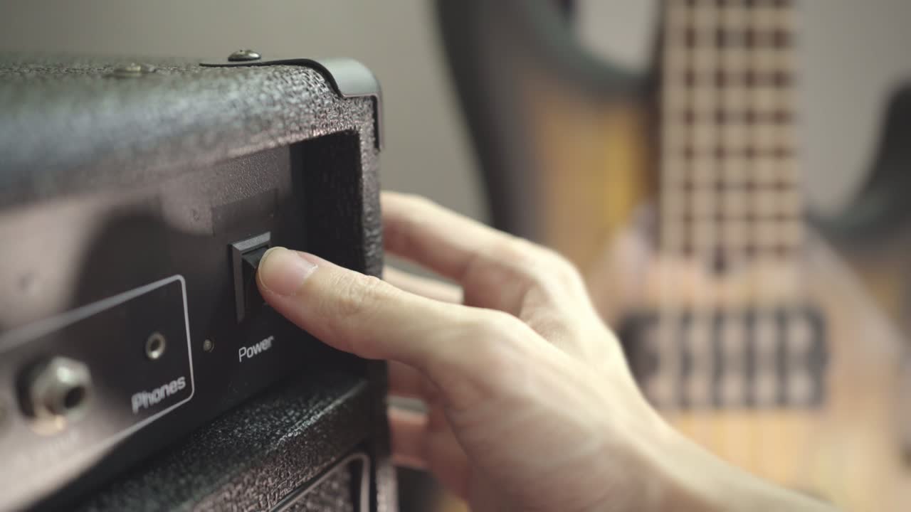 Turn on an amplifier and picking an electric bass guitar from a stand