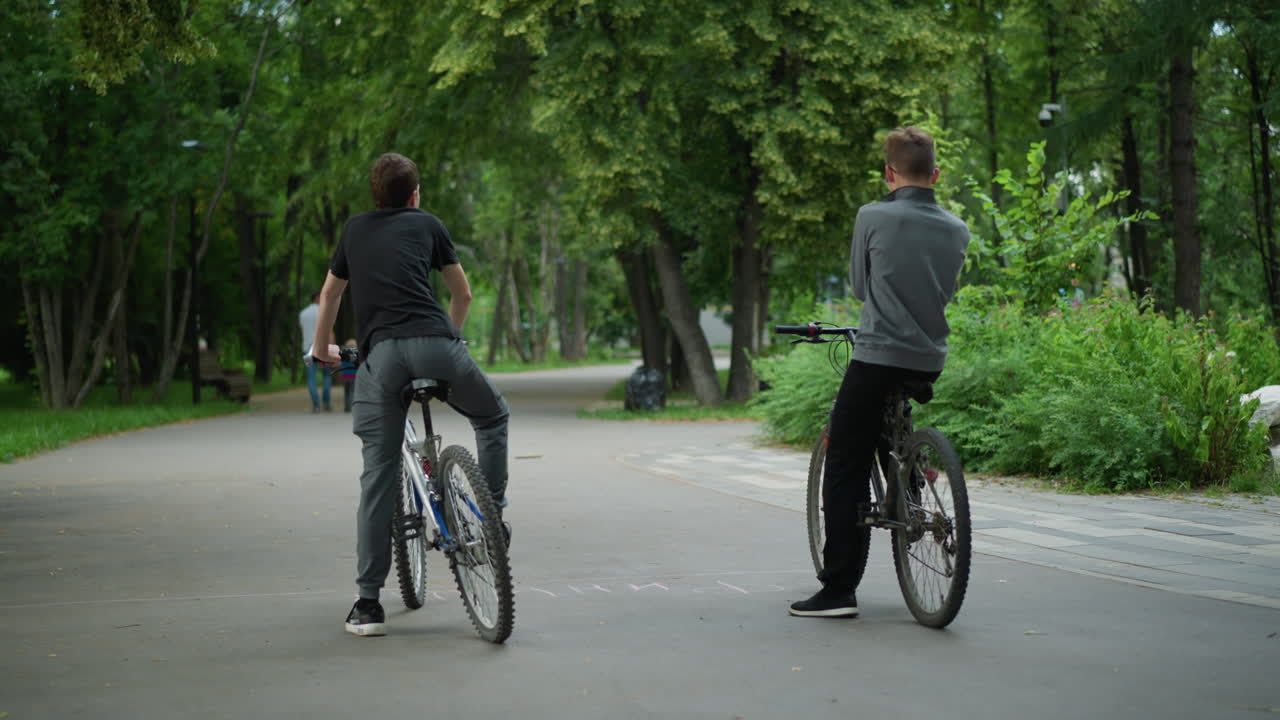 풍경이 아름답고 푸른 공원에서 자전거를 타고 앉아있는 두 친구의 뒷면, 두 라이더는 평온한 분위기로 주변을 바라보면서 휴식을 취합니다.