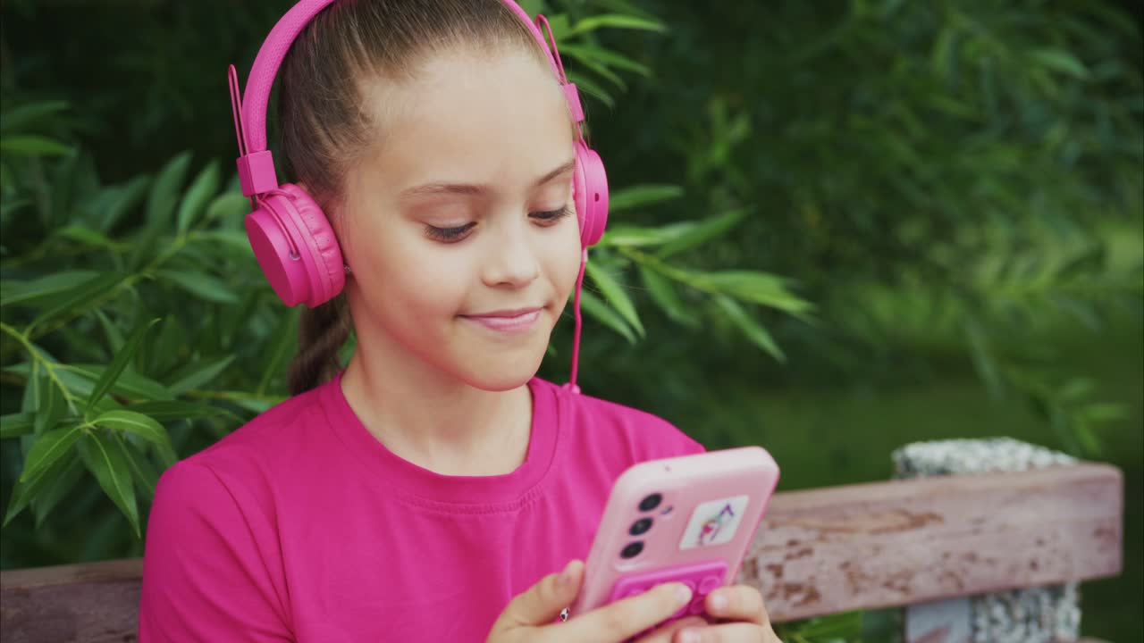 A Young Girl Enjoys Music on Her Smartphone while Relaxing in a Lush Green Park, Showcasing the Joy of Listening to Tunes with Comfortable Headphones