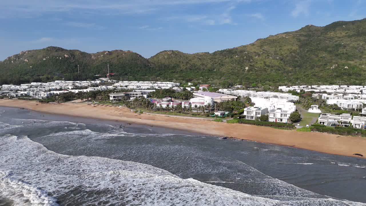 Breathtaking aerial footage of a Vietnam beach showcasing a stunning resort nestled between lush green hills and the sparkling coastline under the bright sunny sky
