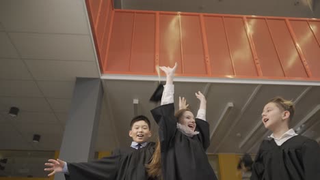 happy multiracial students throwing their mortarboards up in the air. they hug.