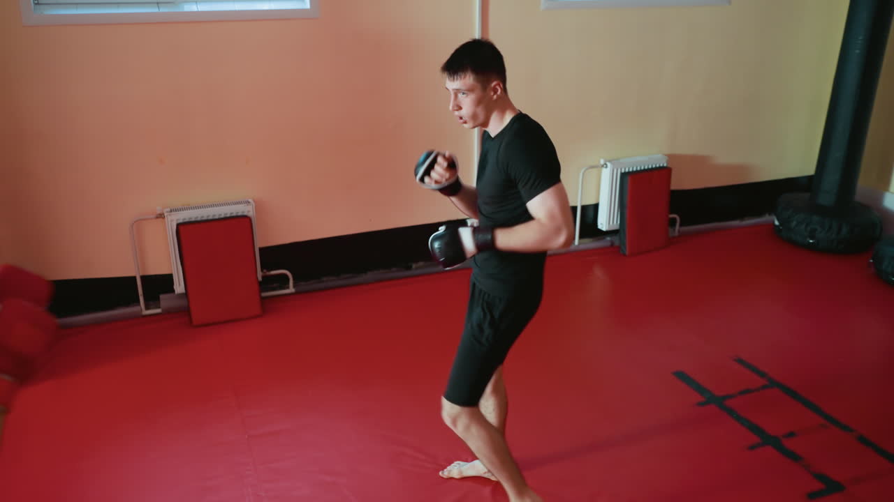 Wrestlers performing boxing pad training inside gym, one athlete in red gloves throwing punch with speed and power while other holds pads, showcasing coordination,discipline, and athletic