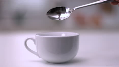 sugar cube falling from teaspoon into a white cup