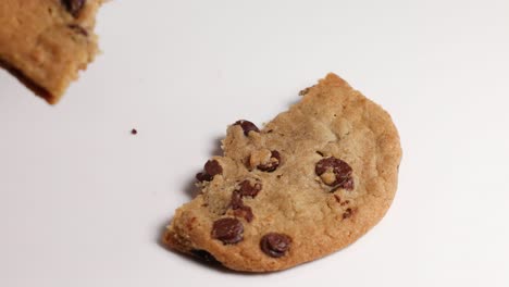 a hand breaks a chocolate chip cookie in half and takes one piece. bright lighting highlights the cookie's texture