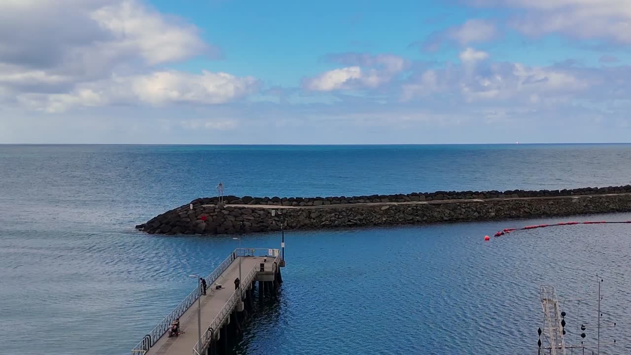 Un filmato di un drone cattura un frangiflutti in pietra e le calme acque blu dell'oceano sotto un cielo nuvoloso