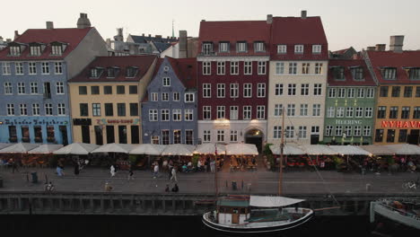 experience the enchanting sunset over nyhavn, copenhagen, where people gather, and boats navigate the charming canal