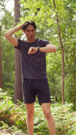 vídeo vertical de un hombre haciendo ejercicio haciendo trabajo al aire libre corriendo a lo largo de una pista en el bosque deteniéndose para respirar y comprobando la actividad aplicación en reloj inteligente disparado en tiempo real 2