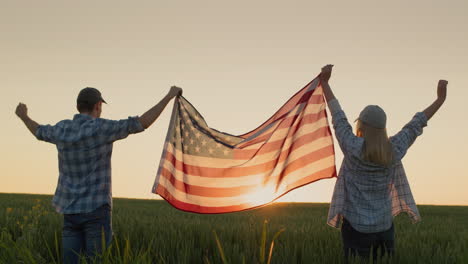 a man and a woman raise the us flag over a field of wheat as the sun sets. usa independence day concept